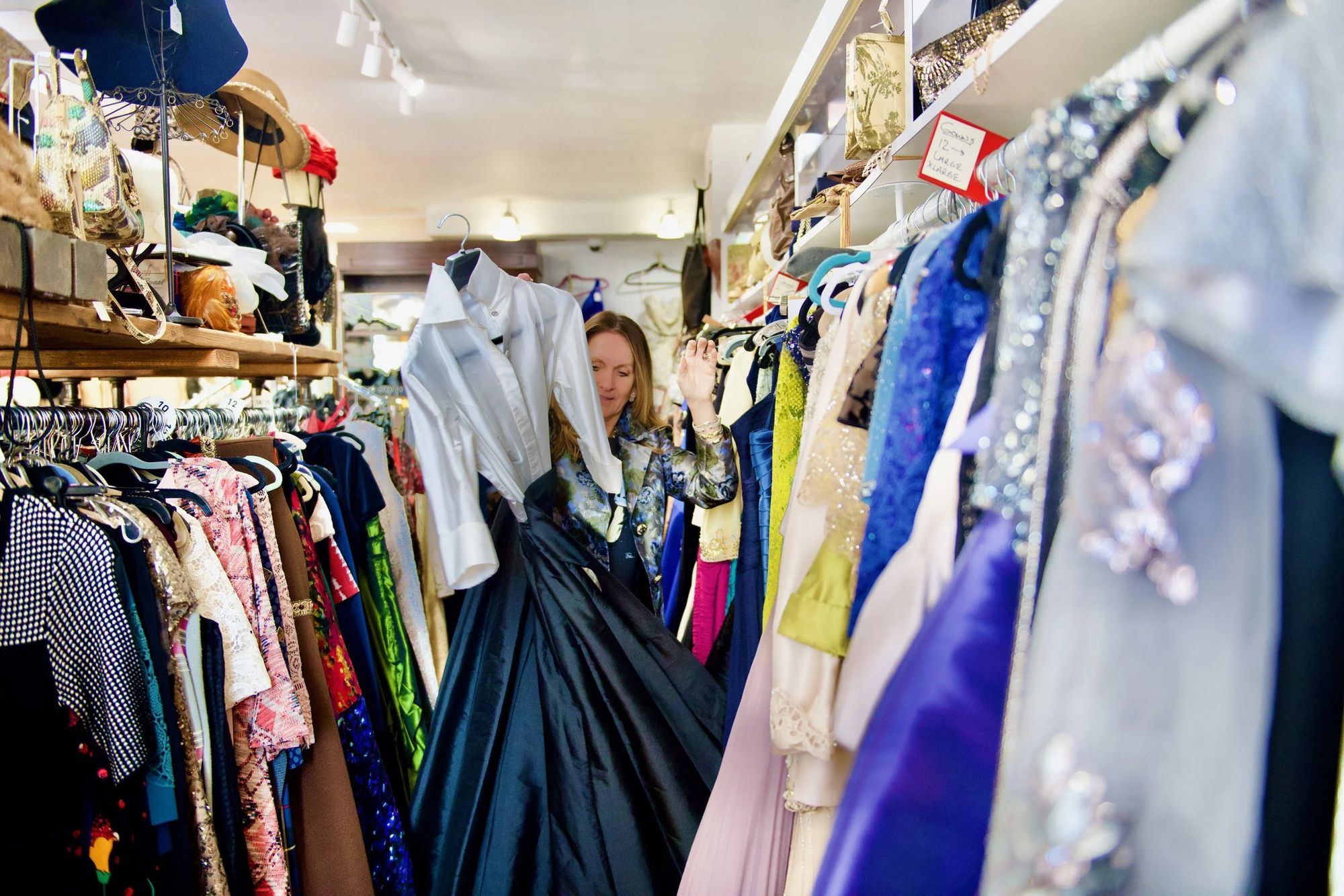 Racks of sequined gowns, satin, lace and prints inside Pure Couture, with hats and handbags on the shelves above