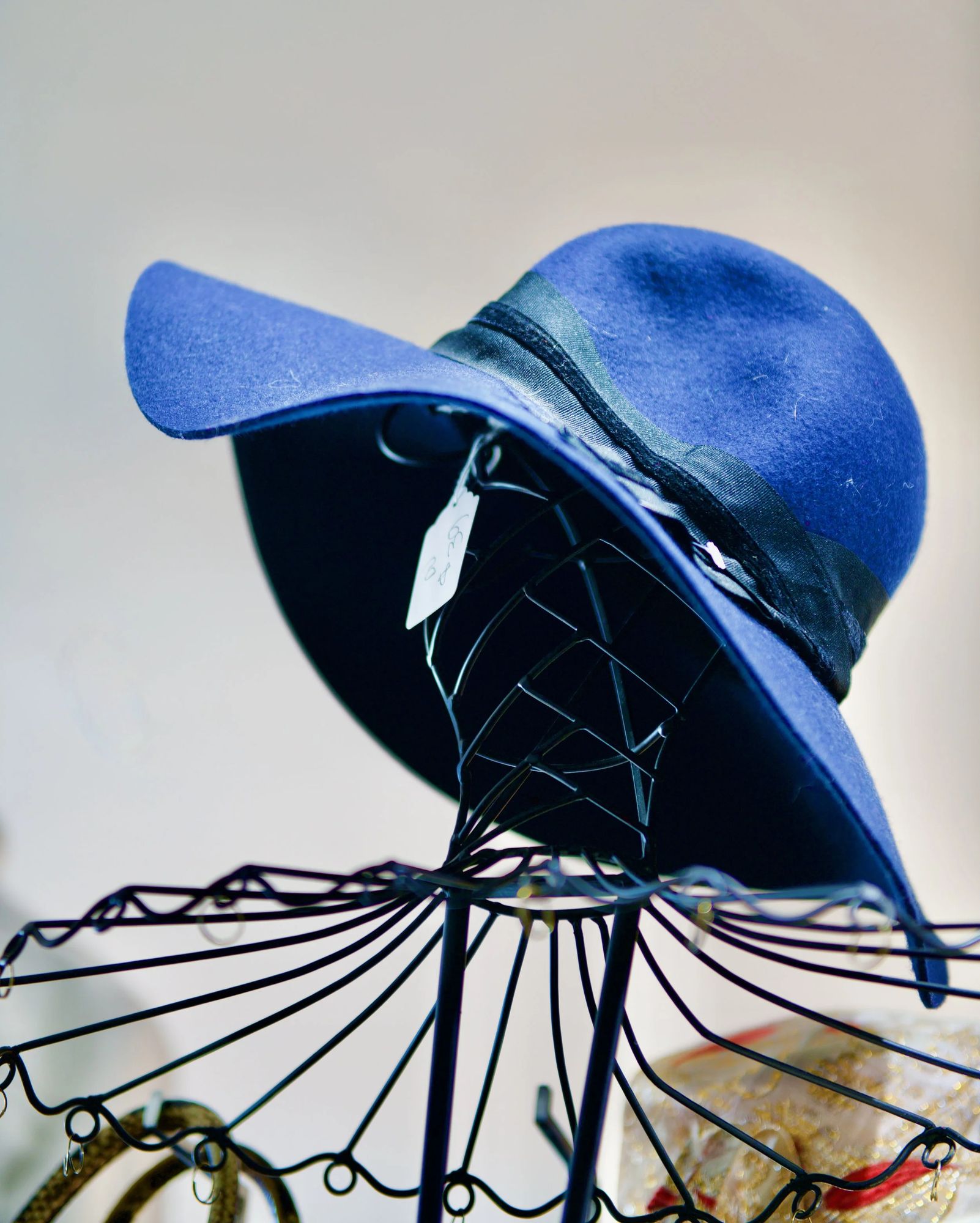 A cobalt wide-brim felt hat on a black wire stand
